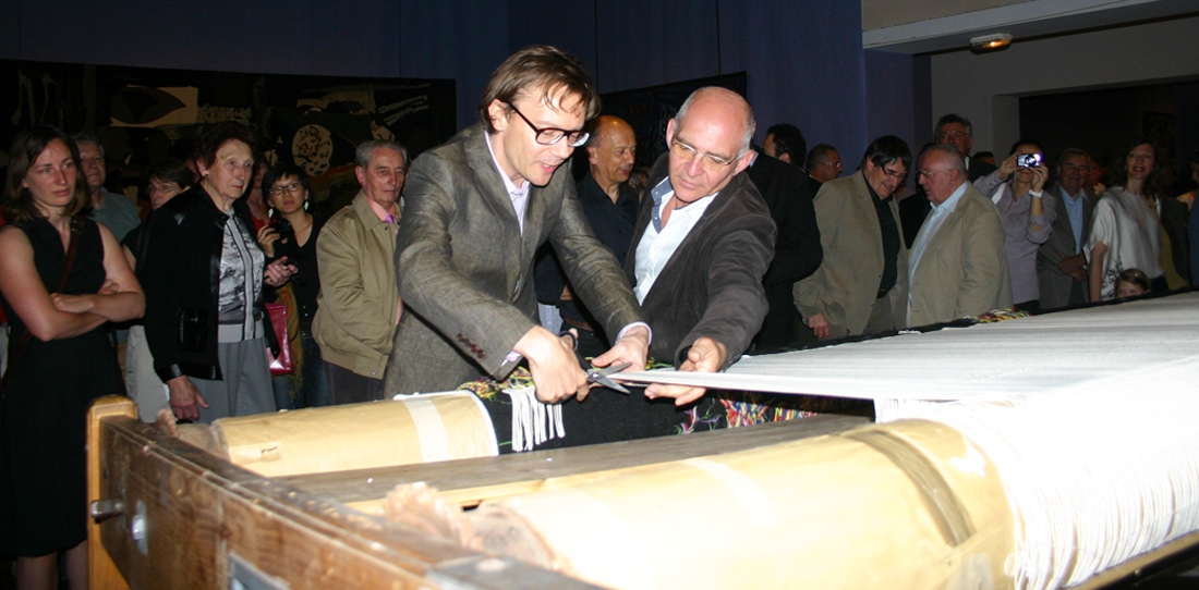 Mathieu Mercier cutting his tapestry off the loom, next to Pascal Legoueix